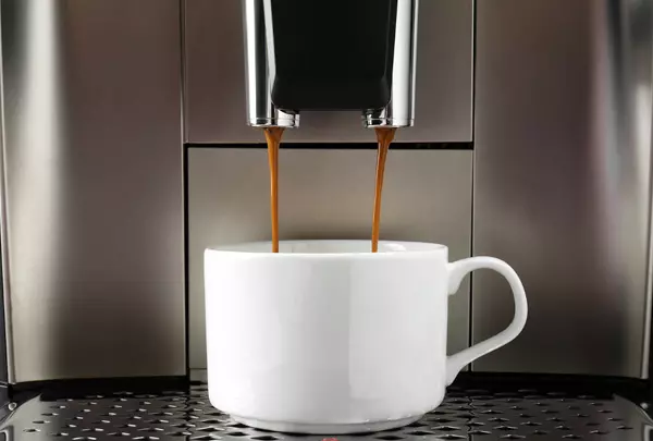 Düsen eines Kaffeevollautomaten befüllen eine weiße Tasse